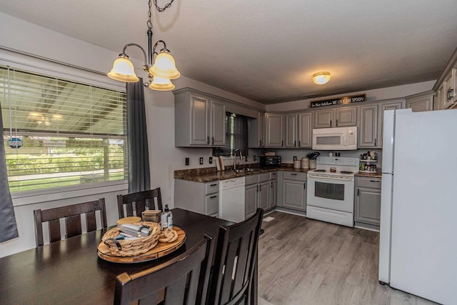 kitchen with dark countertops, an inviting chandelier, a sink, white appliances, and gray cabinets