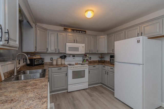 kitchen with white appliances, gray cabinetry, a sink, and light wood-style flooring