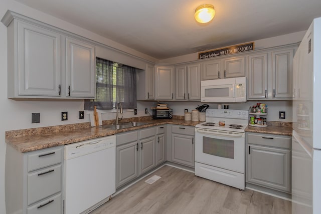 kitchen featuring a sink, gray cabinets, light wood finished floors, and white appliances