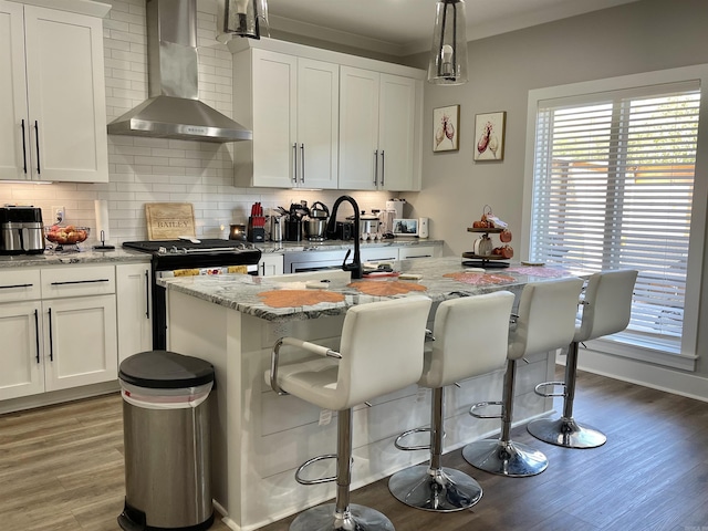kitchen with wall chimney range hood, white cabinets, gas stove, light wood-style flooring, and decorative backsplash