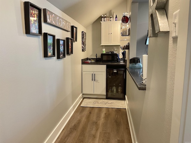 bar with black microwave, dark wood finished floors, baseboards, lofted ceiling, and wine cooler