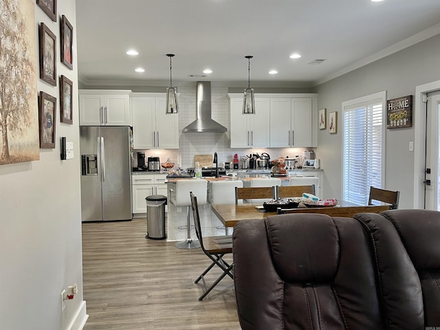 kitchen with stainless steel fridge with ice dispenser, light wood-style floors, wall chimney exhaust hood, backsplash, and ornamental molding