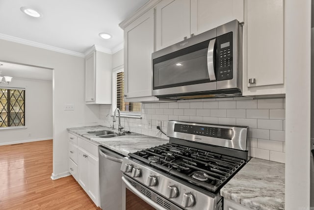 kitchen with a sink, crown molding, stainless steel appliances, and white cabinetry