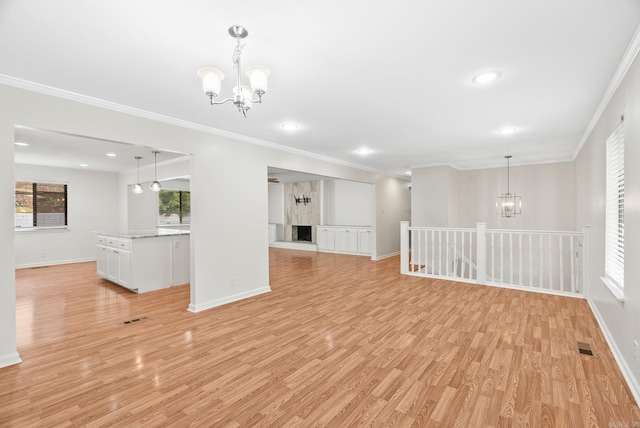 unfurnished living room featuring crown molding, light wood-style flooring, baseboards, and a chandelier