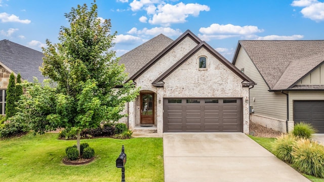 french country inspired facade with a front lawn, roof with shingles, brick siding, an attached garage, and driveway