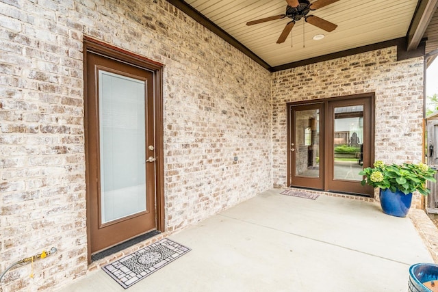 view of exterior entry featuring french doors, ceiling fan, and brick siding