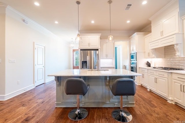 kitchen with visible vents, an island with sink, tasteful backsplash, a sink, and appliances with stainless steel finishes