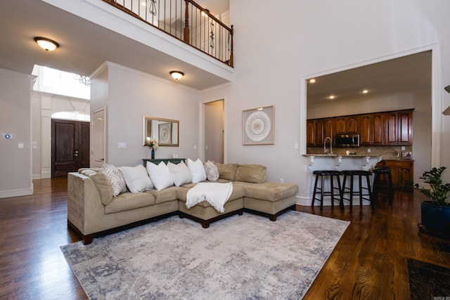living room featuring baseboards, ornamental molding, dark wood finished floors, and a high ceiling