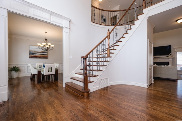 stairway featuring a high ceiling, a chandelier, wood finished floors, and visible vents