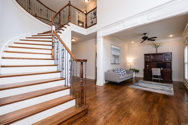 stairs with ceiling fan, ornamental molding, baseboards, and a towering ceiling