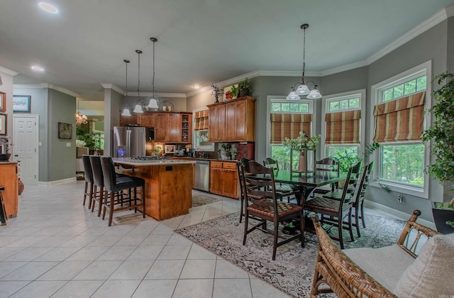 kitchen with appliances with stainless steel finishes, a chandelier, brown cabinetry, light tile patterned floors, and a kitchen island