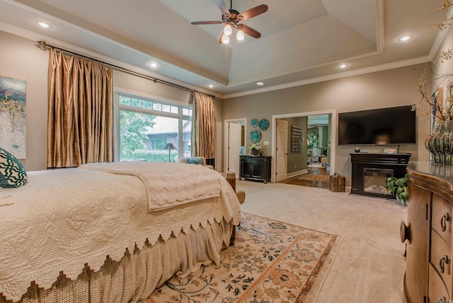 carpeted bedroom featuring crown molding, recessed lighting, a glass covered fireplace, and a raised ceiling