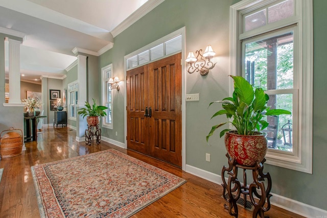 entryway featuring baseboards, ornamental molding, decorative columns, and wood finished floors