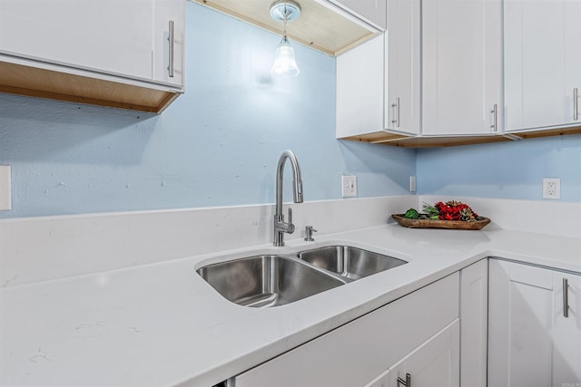 kitchen with light countertops, white cabinetry, hanging light fixtures, and a sink