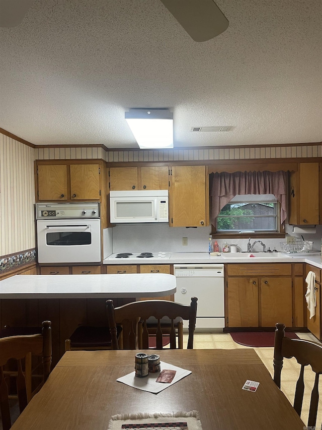 kitchen featuring white appliances, light countertops, a textured ceiling, brown cabinets, and a sink