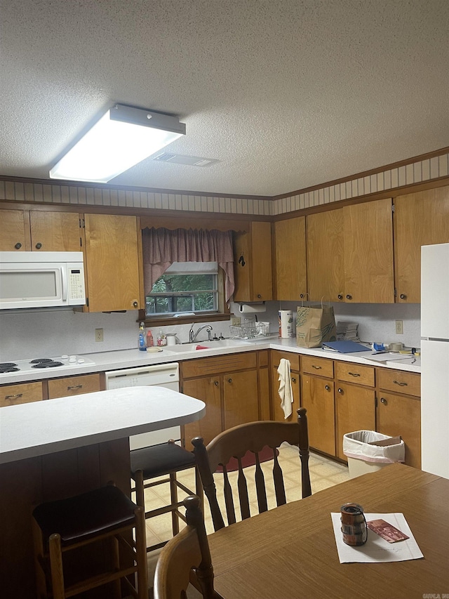 kitchen with a sink, a textured ceiling, white appliances, and light countertops