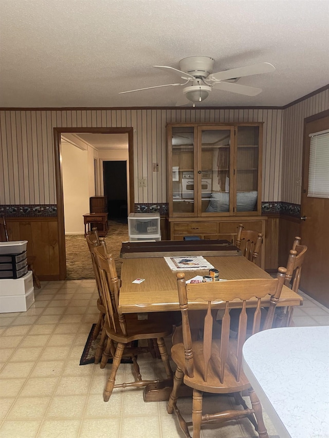 dining area with wainscoting, light floors, ceiling fan, wallpapered walls, and a textured ceiling
