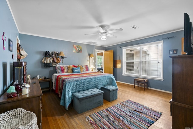 bedroom with a ceiling fan, visible vents, wood finished floors, baseboards, and ornamental molding