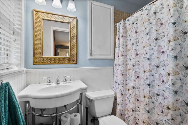 full bathroom featuring a sink, a wainscoted wall, toilet, and curtained shower