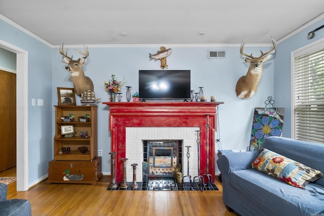 living room featuring visible vents, a brick fireplace, wood finished floors, baseboards, and ornamental molding