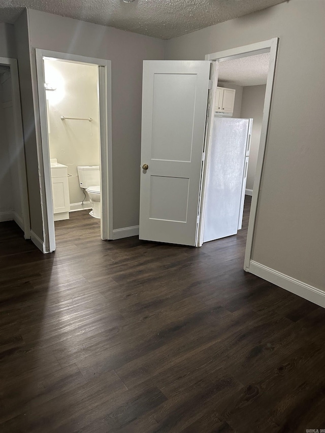 unfurnished bedroom featuring a textured ceiling, dark wood finished floors, baseboards, and ensuite bath
