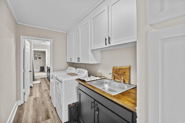 washroom with washing machine and dryer, cabinet space, a sink, baseboards, and light wood finished floors