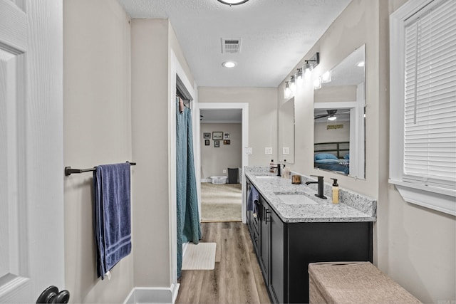 ensuite bathroom featuring a sink, baseboards, wood finished floors, and visible vents
