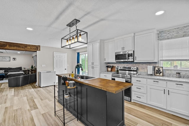 kitchen with stainless steel appliances, butcher block counters, a sink, and white cabinetry