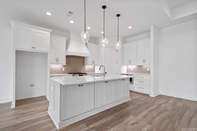 kitchen with a sink, light wood-style flooring, white cabinetry, decorative backsplash, and custom exhaust hood