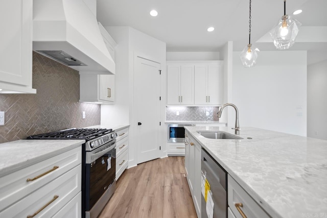 kitchen with light stone counters, white cabinets, custom range hood, a sink, and stainless steel appliances