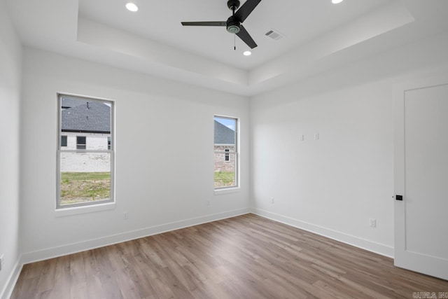 unfurnished room with a ceiling fan, visible vents, wood finished floors, baseboards, and a tray ceiling