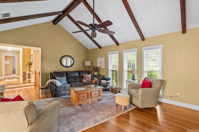 living area featuring visible vents, beam ceiling, baseboards, hardwood / wood-style flooring, and a ceiling fan