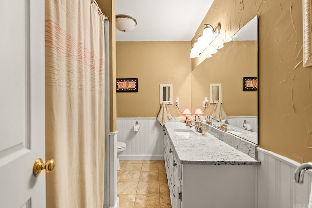full bathroom with vanity, tile patterned floors, a wainscoted wall, and toilet