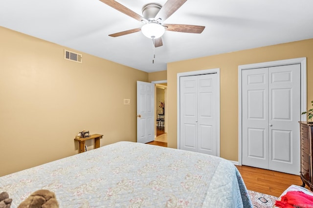 bedroom with two closets, ceiling fan, visible vents, and wood finished floors