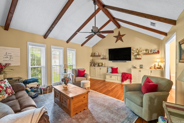 living area with ceiling fan, lofted ceiling with beams, a textured ceiling, wood finished floors, and visible vents