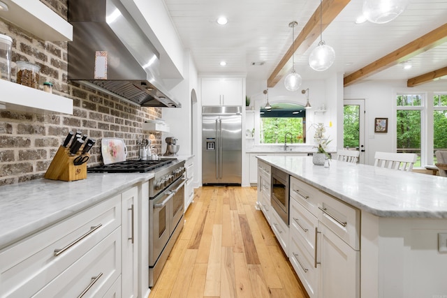 kitchen with light stone countertops, white cabinets, light wood finished floors, built in appliances, and wall chimney exhaust hood