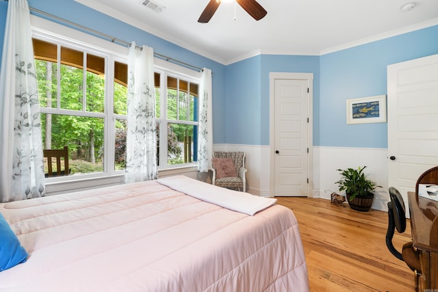 bedroom with ceiling fan, wainscoting, wood finished floors, visible vents, and ornamental molding