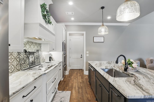 kitchen featuring backsplash, appliances with stainless steel finishes, a center island with sink, a sink, and white cabinetry