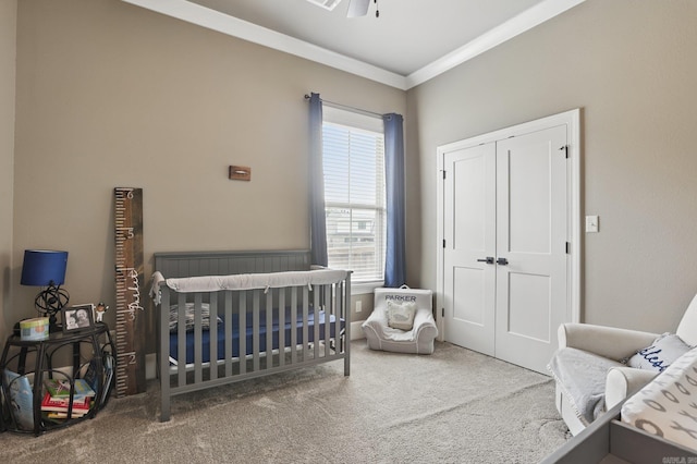 carpeted bedroom with crown molding, a crib, and a closet