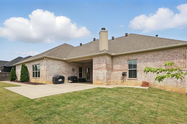 rear view of house featuring brick siding, a yard, a chimney, and a patio
