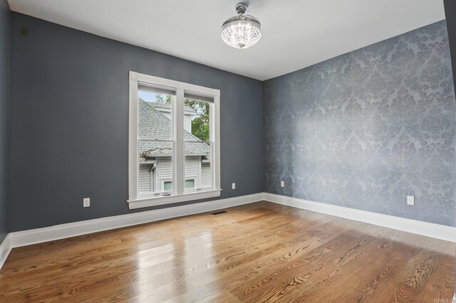 spare room with visible vents, wood finished floors, baseboards, a notable chandelier, and an accent wall