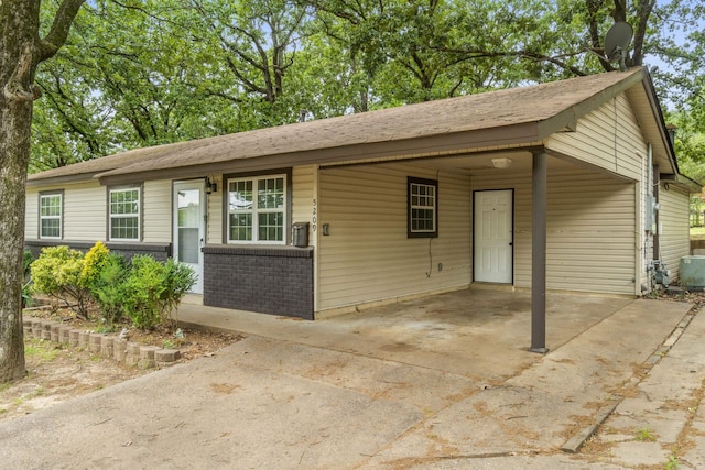 view of front facade with roof with shingles, a carport, driveway, and brick siding