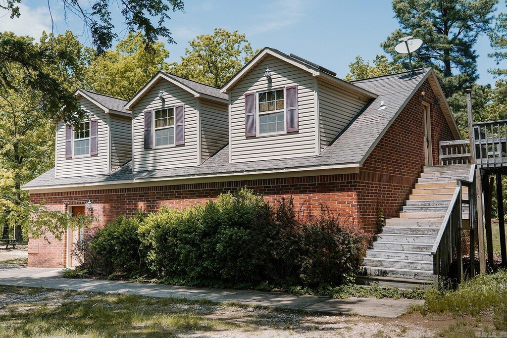 view of front of home with brick siding, roof with shingles, a wooden deck, and stairway