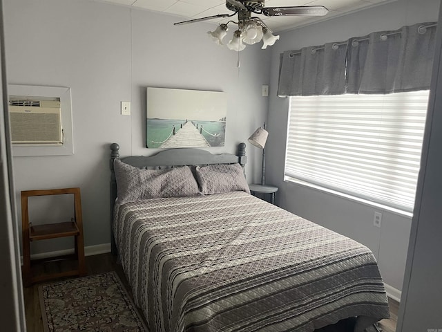 bedroom featuring baseboards, a ceiling fan, wood finished floors, and an AC wall unit