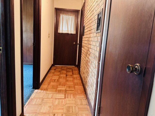hallway featuring baseboards and brick wall