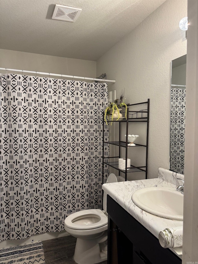 bathroom with a textured wall, vanity, toilet, wood finished floors, and visible vents