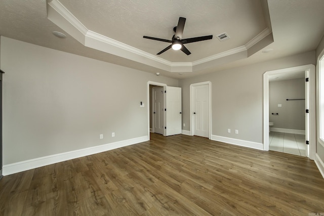 unfurnished bedroom featuring visible vents, crown molding, wood finished floors, baseboards, and a tray ceiling