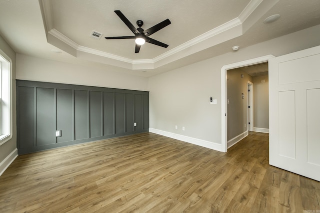 unfurnished bedroom featuring attic access, visible vents, crown molding, wood finished floors, and a raised ceiling