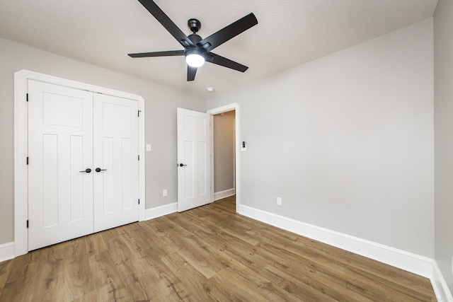 unfurnished bedroom featuring baseboards, light wood-style flooring, ceiling fan, and a closet