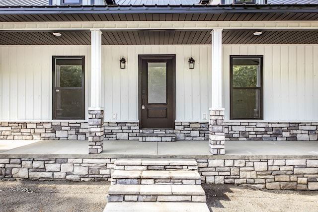doorway to property featuring a porch, metal roof, and stone siding